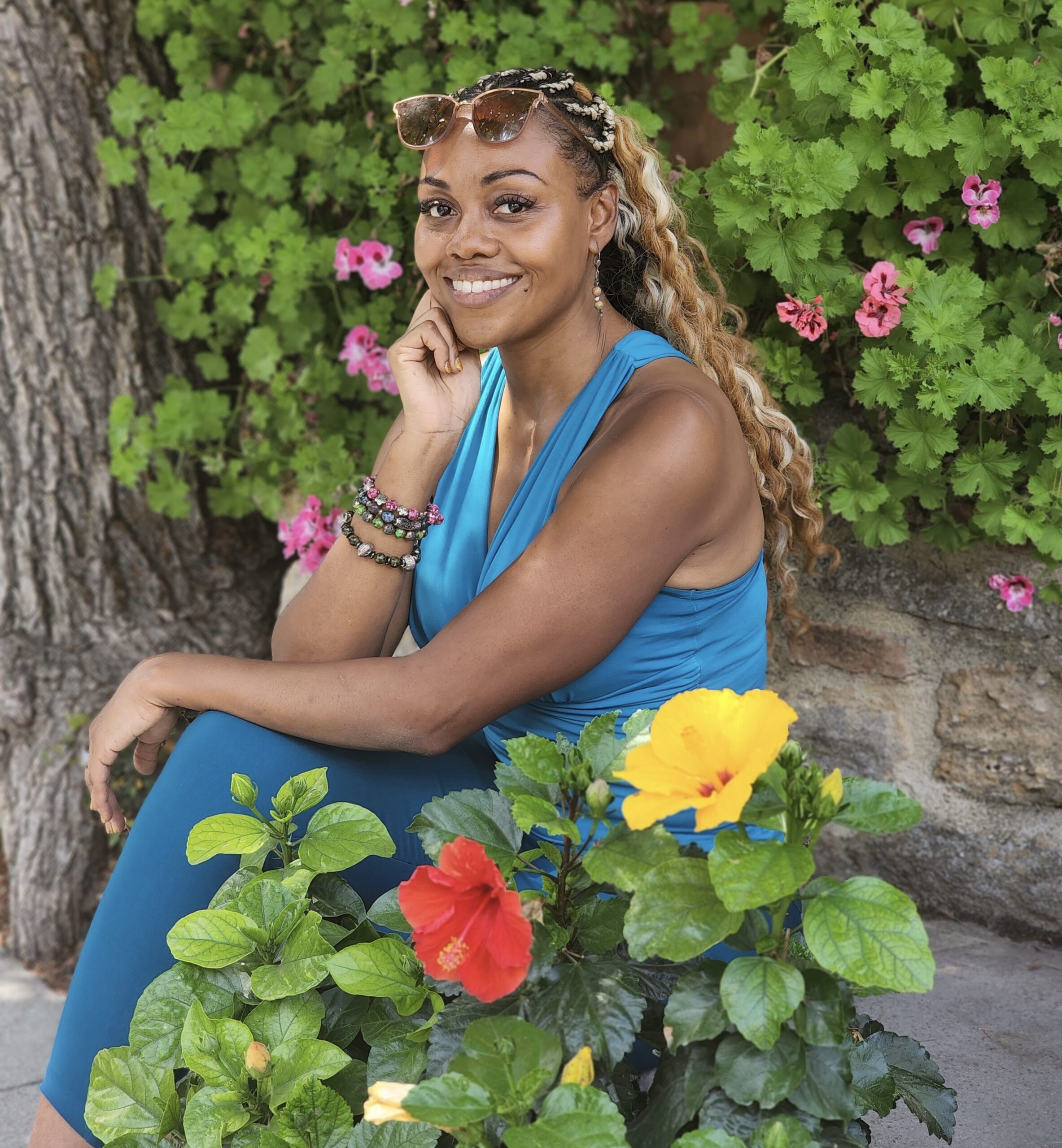 A woman with long hair smiles among vibrant garden flowers.