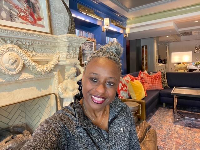Smiling woman with braided hair sitting in a cozy, colorful living room.